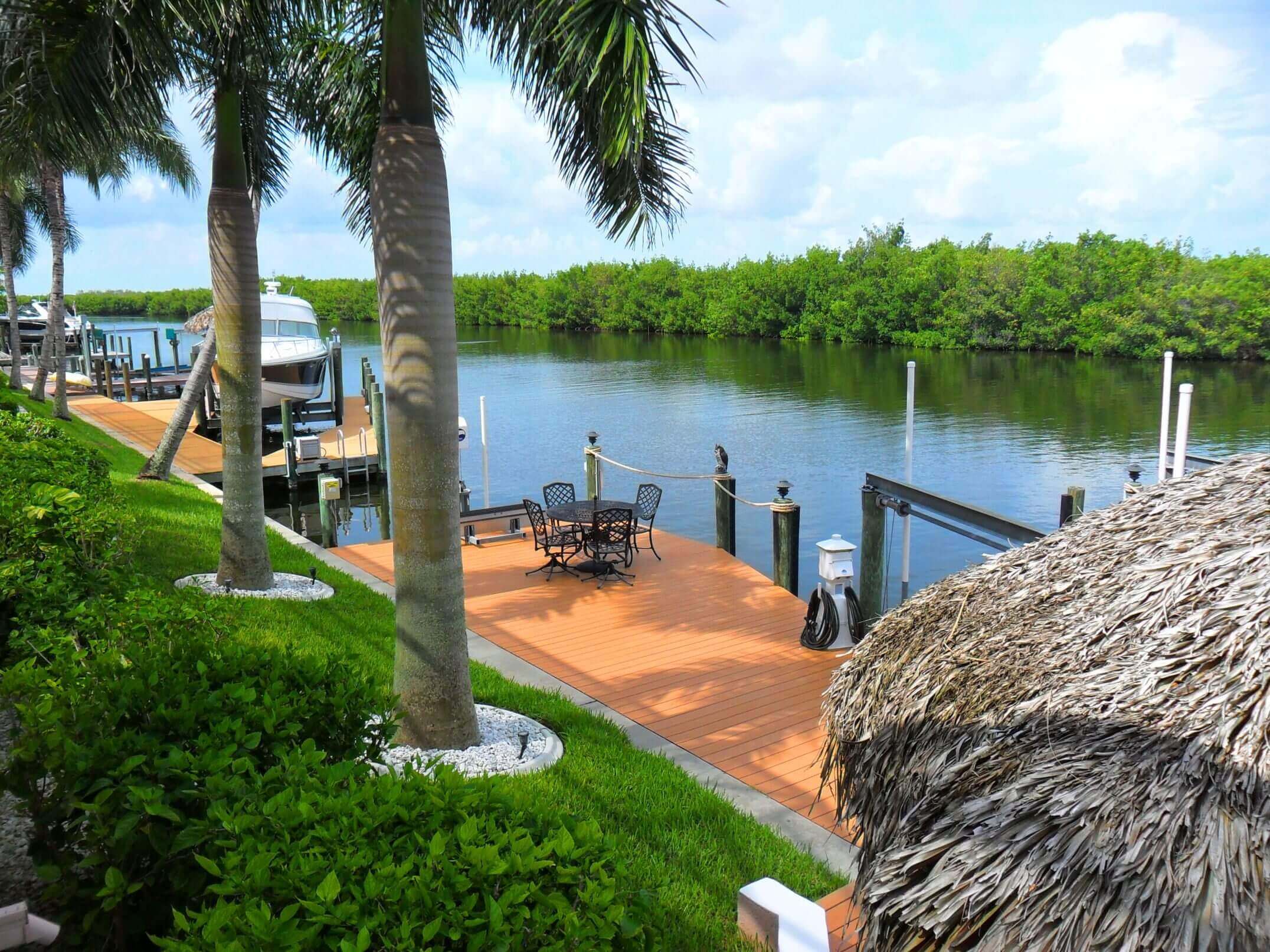 A dock with palm trees and chairs on the water.