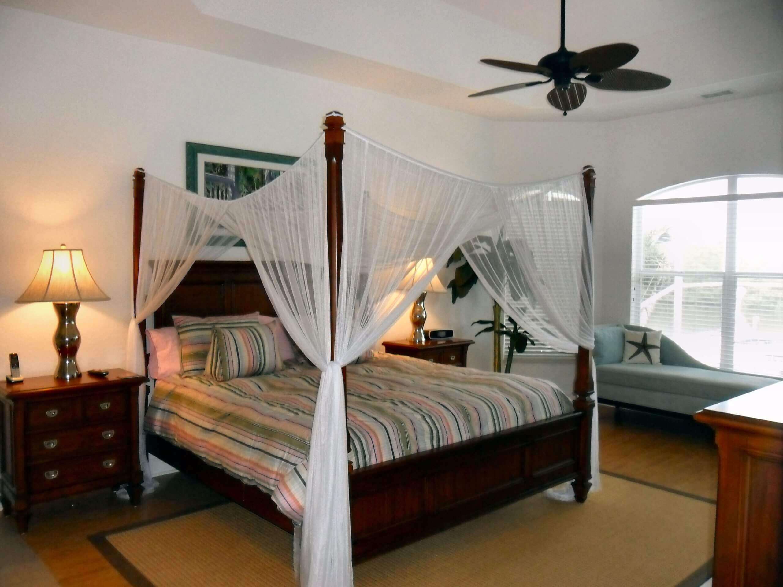 A bedroom with four poster bed and white curtains.
