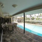 A patio with chairs and tables next to the pool.