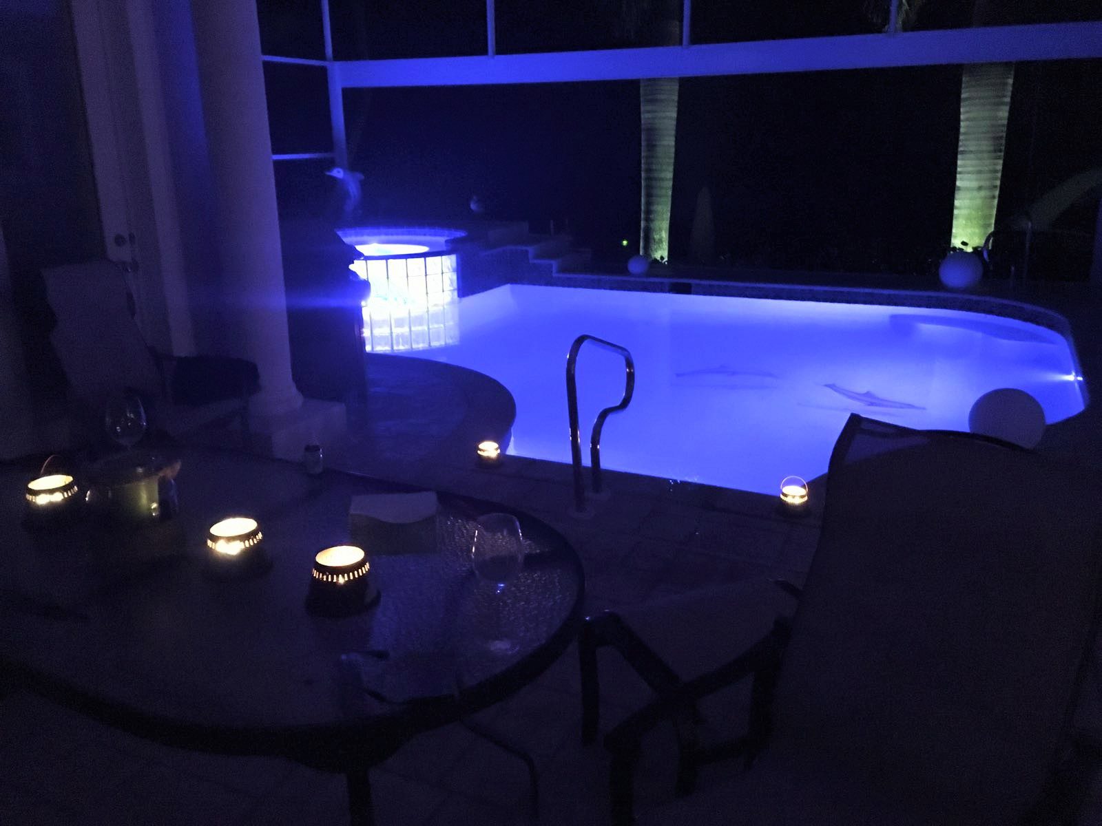 A table with two chairs and candles in front of an indoor pool.